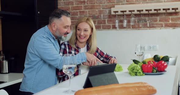 Man Standing Behind His Smiling Lovely Wife and Helping Her to Cut Cucumber for Vegetable Salad