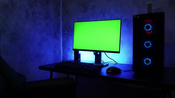 Blank green screen desktop computer on the table with RGB led lights in the dark room