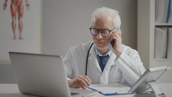 Male Doctor Using Telephone While Working at Table in Clinic