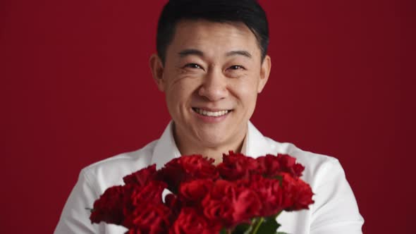 Pretty Asian man in white shirt holds out a bouquet of red roses to the camera