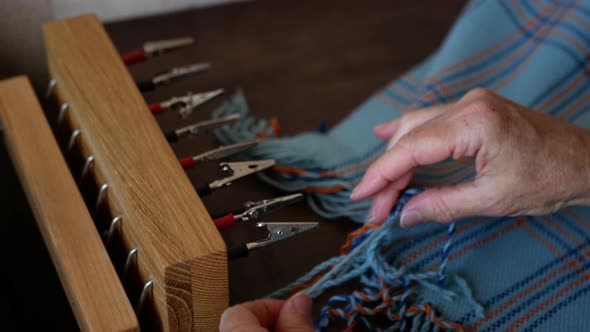 Woman is creating a fringe on a handmade scarf or shawl using special tool