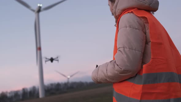 Female Engineer Uses a Drone to Check a System Performance of Wild Turbine or Windmill at Sunset