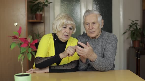 Pretty Mature Senior Couple Grandparents Enjoy Online Shopping on Phone at Home