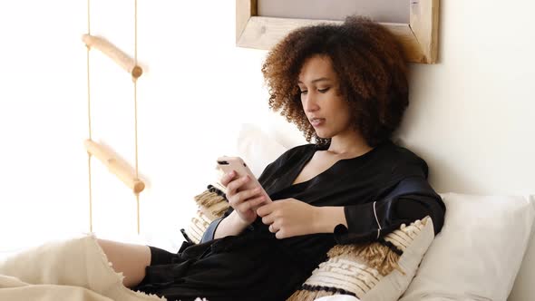 Young Beautiful African American Woman Texting on Smartphone or Watching Social Network