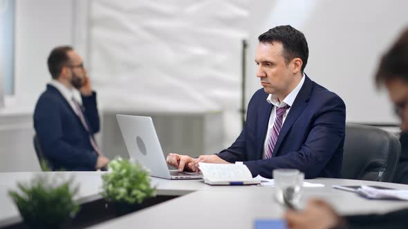 Focused Businessman in Suit Enjoying Job Sitting on Desk at White Room Interior RED Raven Camera