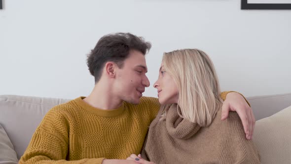 Happy Affectionate Young Couple Bonding Talking Hugging at Home on Sofa