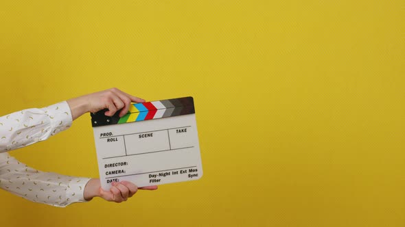 Hands Holding a Clapper Board on a Yellow Isolated Background