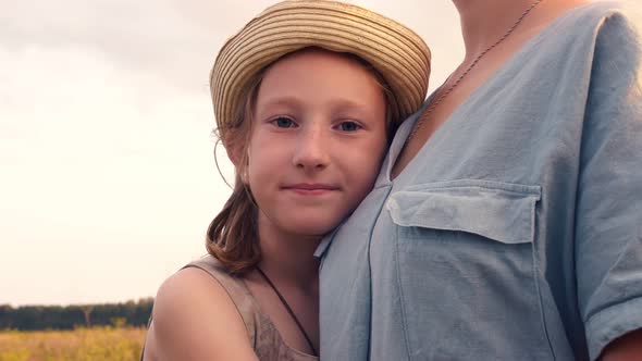 A Teenage Girl in a Hat with Blond Hair and Blue Eyes Hugs Her Mother Tightly