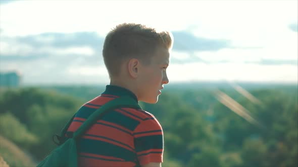 Teenager in a Red Shirt with a Backpack on His Back, at Sunset, Sitting on a High Hill and Looking