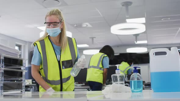 Woman wearing hi vis vest and face mask cleaning the office using disinfectant