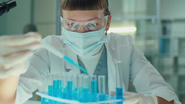 Female Microbiologist in Mask and Gloves Working with Blue Liquid in Lab