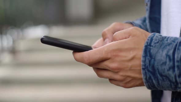 Closeup Hands of Man Texting Message on Mobile Phone Outdoors on Blurred Background Side View