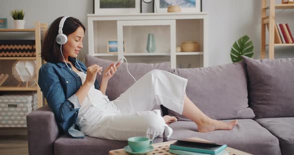 Cheerful Girl Using Smartphone and Listening To Music in Modern Headphones