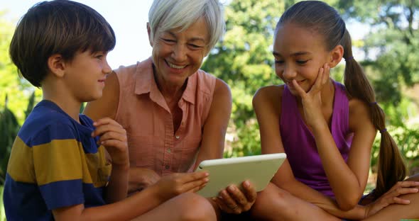 Grandmother and grand kids using digital tablet in the park 4k