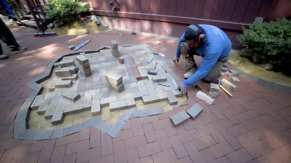 Camera rotates around a brick paver emblem under construction as artist comes over with a cut brick