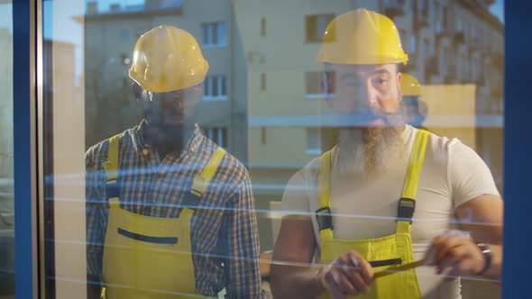 View From Outside of Two Diverse Builders Measuring Window with Tape