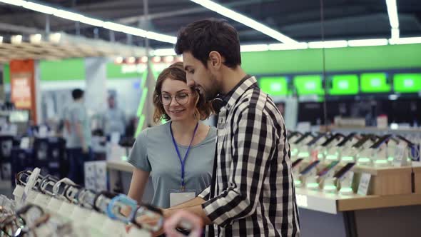 In the Electronics Store Female Consultant Gives Professional Advice to a Young Man