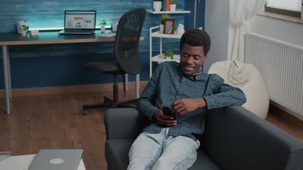 African American Man with Phone in Hands Looking at Online Streaming Services Content