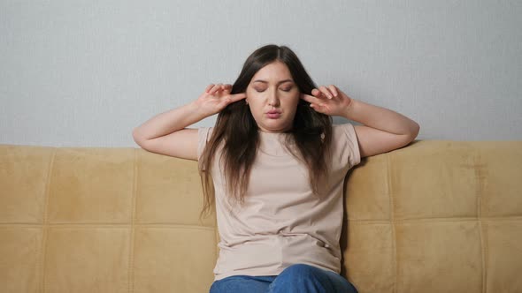 Woman Covers Her Ears and Swears at the Noise From Neighbors While Sitting on the Couch