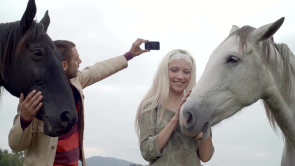 Young Man and Woman Friends Make a Selfie with White and Black Horses Outdoor Gimbal Steadicam Slow