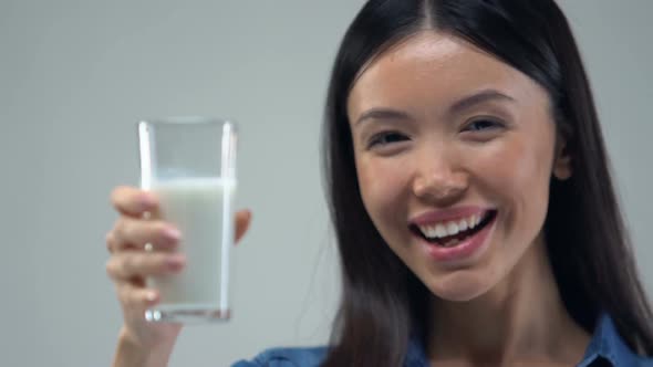 Smiling Asian Girl Showing Glass of Milk Into Camera