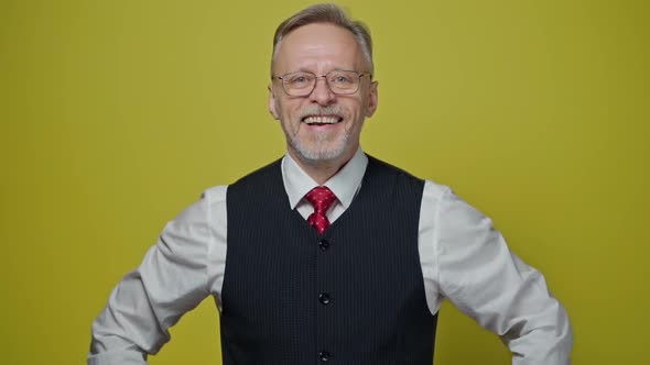 Portrait of smiling old businessman. Mature man in glasses laughing on camera on yellow background. 