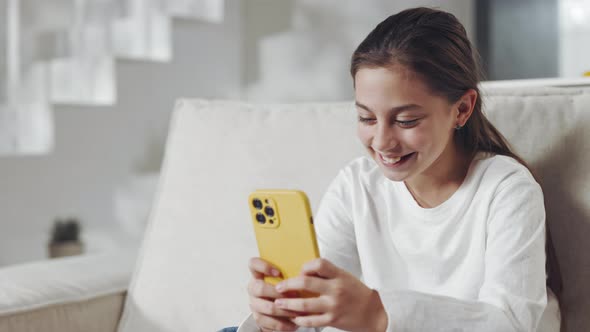 Smiling Caucasian Child Using Mobile While Relaxing on Sofa