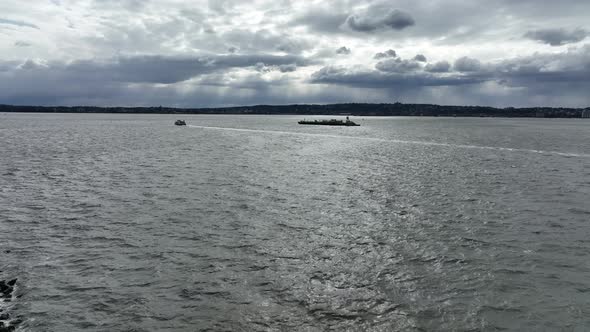 An aerial view of a barge and a ferry sailing in the waters of Upper Bay, New York on a cloudy day.