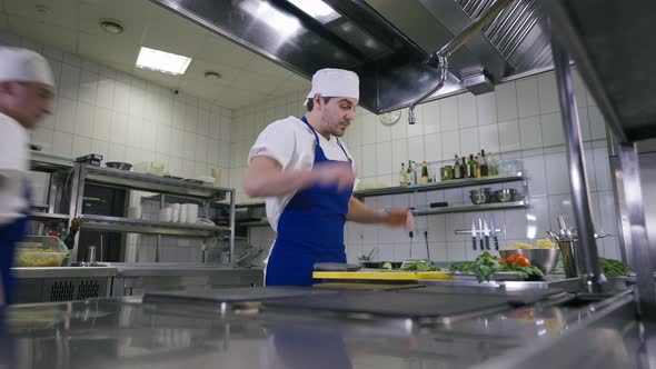 Tired Young Handsome Cook Standing in Kitchen Wiping Forehead As Colleague Entering