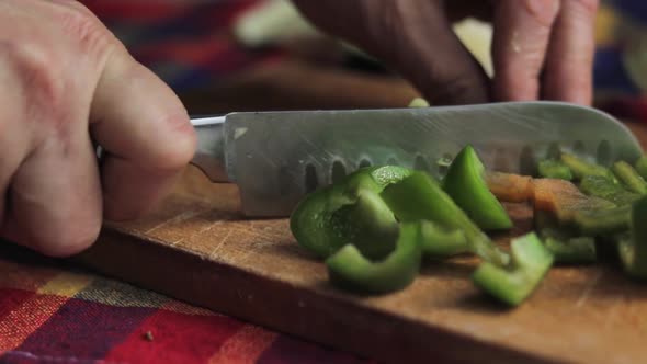 Extreme close up and low angle view of a santoku knife slicing a green sweet pepper on a wooden cutt