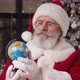 Pensive Santa Sitting By a Christmas Tree in His Residence Turning a Globe in His Hands Looking - VideoHive Item for Sale