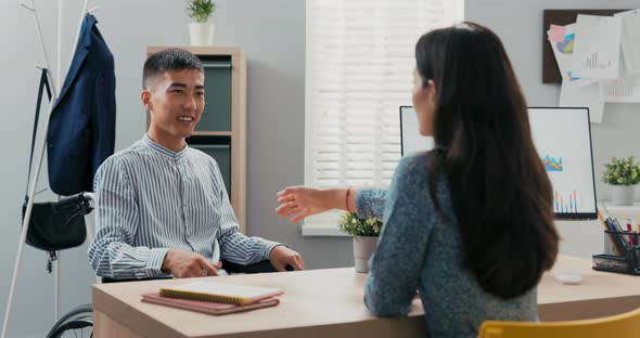 Man Sits in Wheelchair at Desk in an Office Opposite Him Beautiful Woman in Dress Asks Questions