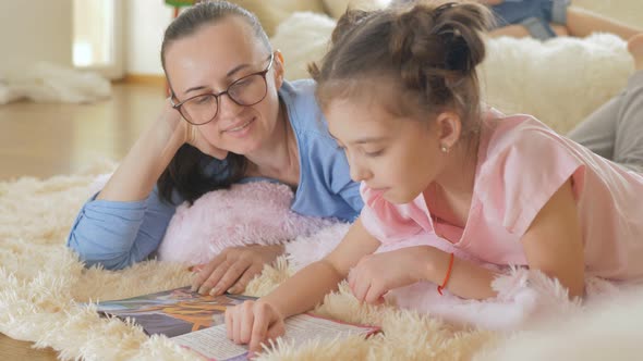 A Teenage Girl Reads a Children's Book with Her Mother Lying on the Floor in the Room