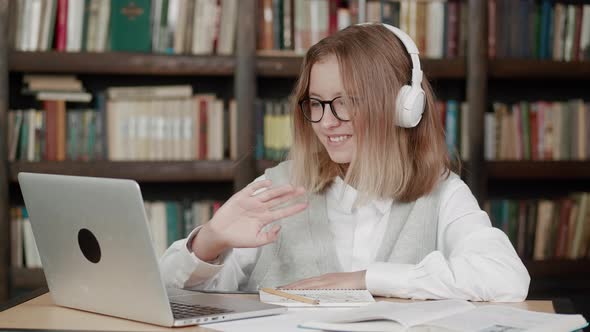 Smart Teen Girl School Pupil Wear Headphones Learning Online with Teacher Tutor Waving Hand Using