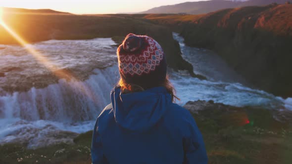 Rear View of Young Woman in Hat Looking at Waterfall During Sunset Slow Motion