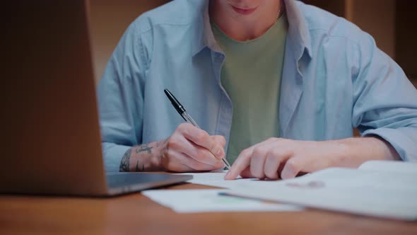 Closeup Shot of Young Man Studying Writing Notes and Looking at the Laptop