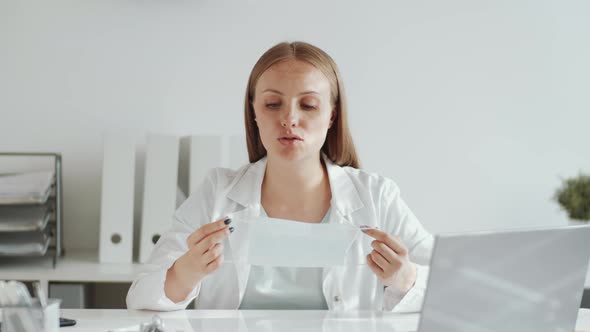 Female Doctor Demonstrating How to Wear Medical Face Mask at Camera