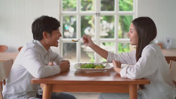 Sweet asian couple enjoy to feed salad to her boyfriend while on date in restaurant