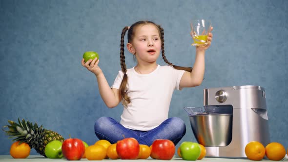 Girl with glass of orange juice. Little girl eating apple with homemade juice