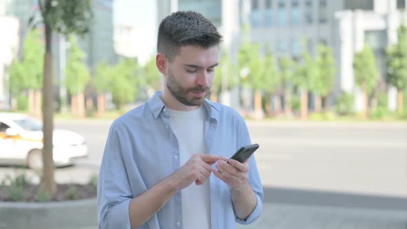 Young Man Celebrating Online Success on Smartphone Outdoor