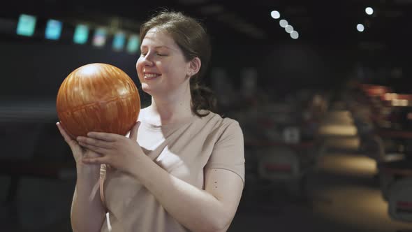 Portrait of Simple Happy Young Woman with Orange Ball in a Bowling Alley