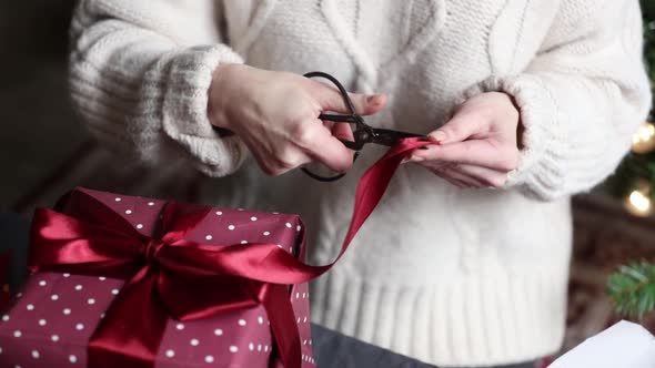 Woman cut ribbon and wrapping a Christmas gifts on a table