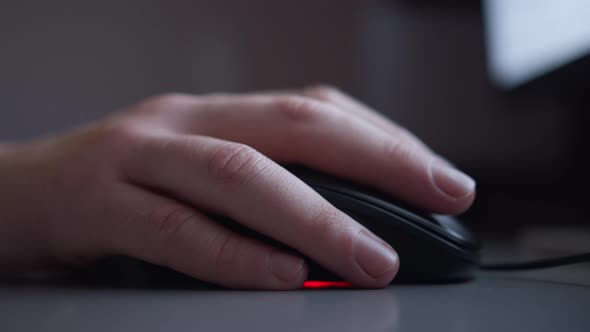 Hand on a computer mouse, works in the evening behind the monitor, backlight from the monitor screen