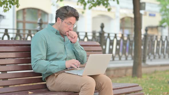 Man Coughing while using Laptop on Bench