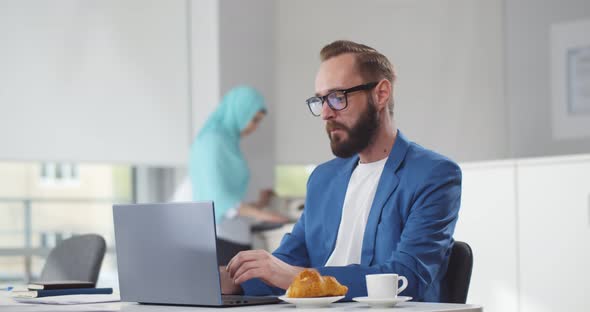 Handsome Entrepreneur Eating Pastry and Working on Laptop in Coworking Space