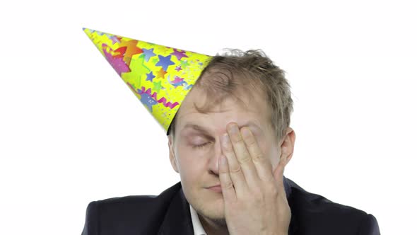 Drunk Sleepy Young Businessman with Hangover in Festive Cap Rubs His Eyes