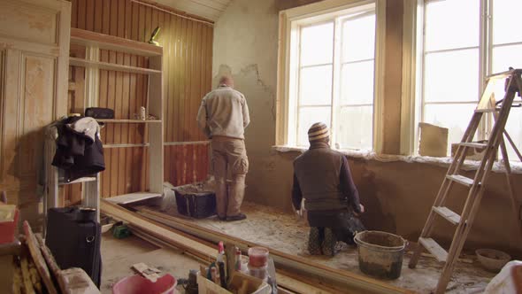 TRACKING shot R2L ZOOM OUT of 2 men plastering walls with clay, DIY