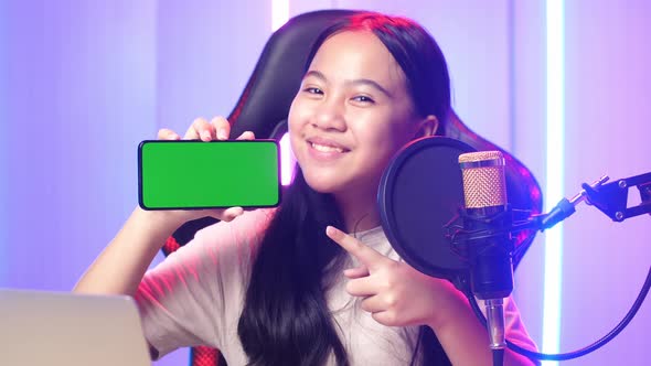 Asian Kid Girl Holding Mobile Phone With Mock Up Green Screen While Live Stream alt