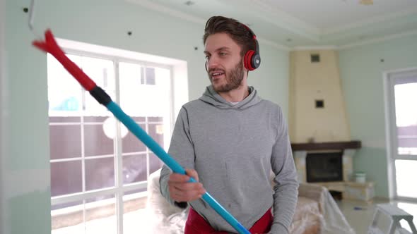 Joyful Man in Headphones Dancing Painting Wall in New Home Indoors