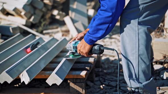 Laborer polishes stone with hand grinder outdoors.